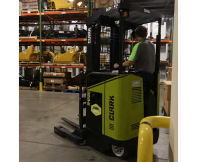 Operator driving a Clark NPX 17 order picker through a warehouse, with industrial racking, palletized inventory, and equipment stored throughout the facility.