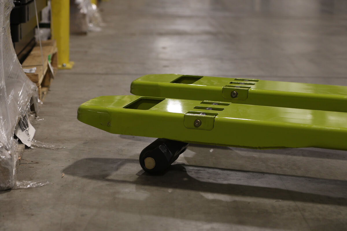 Close-up of the fork tips and load wheels on a Clark electric pallet truck, highlighting the low-profile fork design used for smooth pallet entry and material handling in warehouse environments.